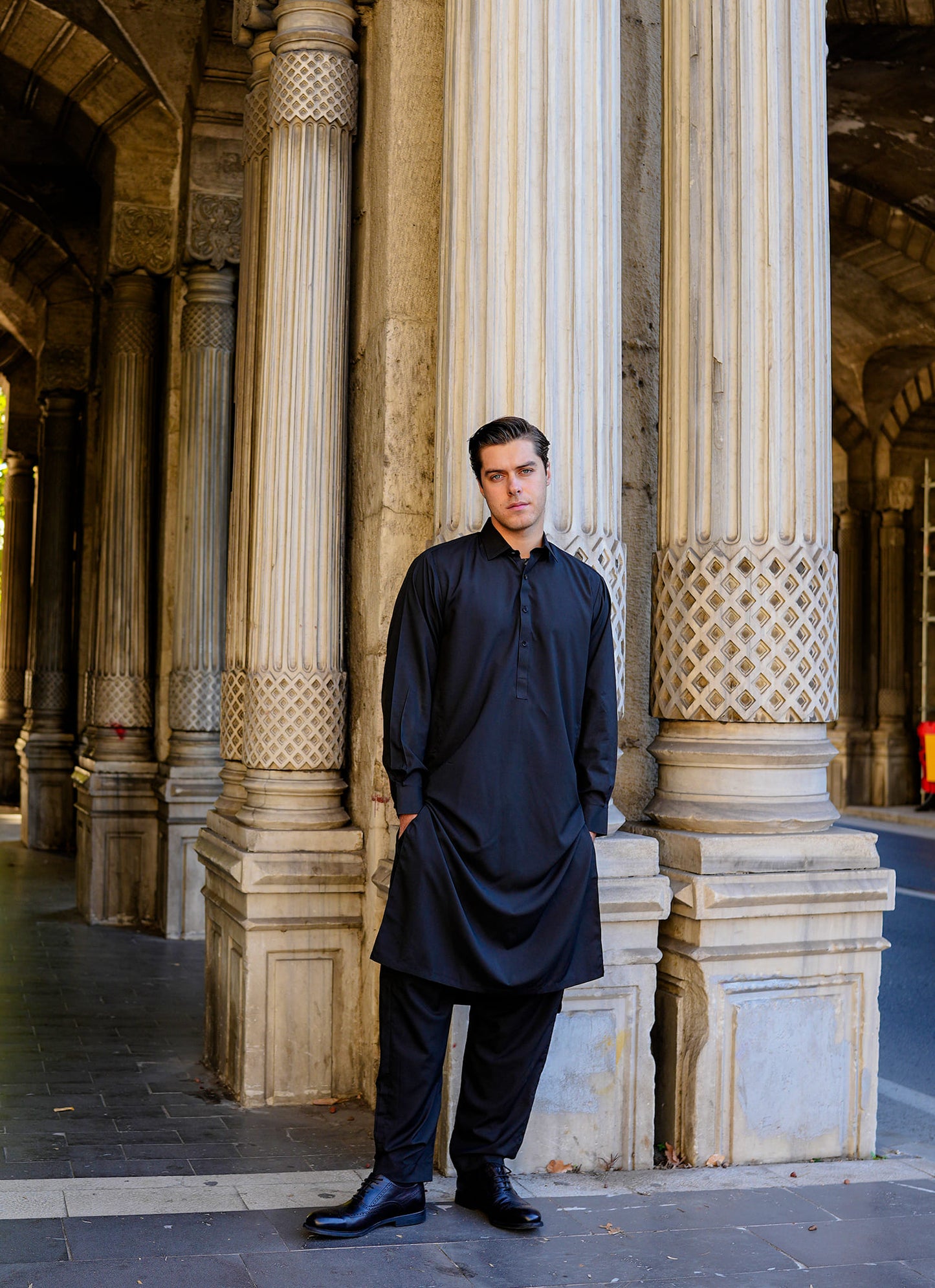 Sheikh Gulzar Fabrics Istanbul Noir — model in black shalwar kameez near mosque pillars, premium traditional men’s fabric Pakistan.