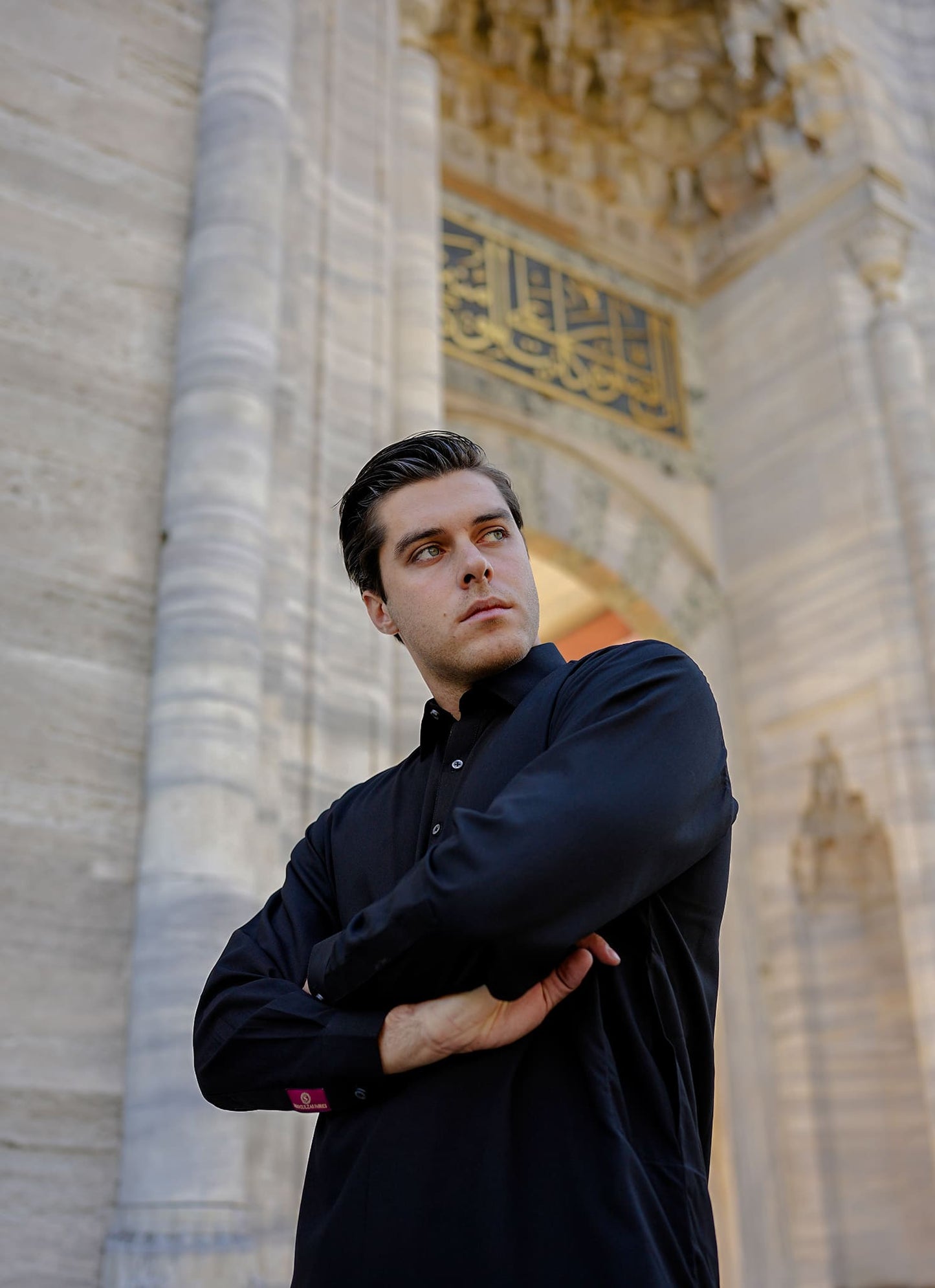 Sheikh Gulzar Fabrics Midnight Shine — premium black unstitched fabric styled on model leaning on wall, luxury men’s fabric Pakistan.