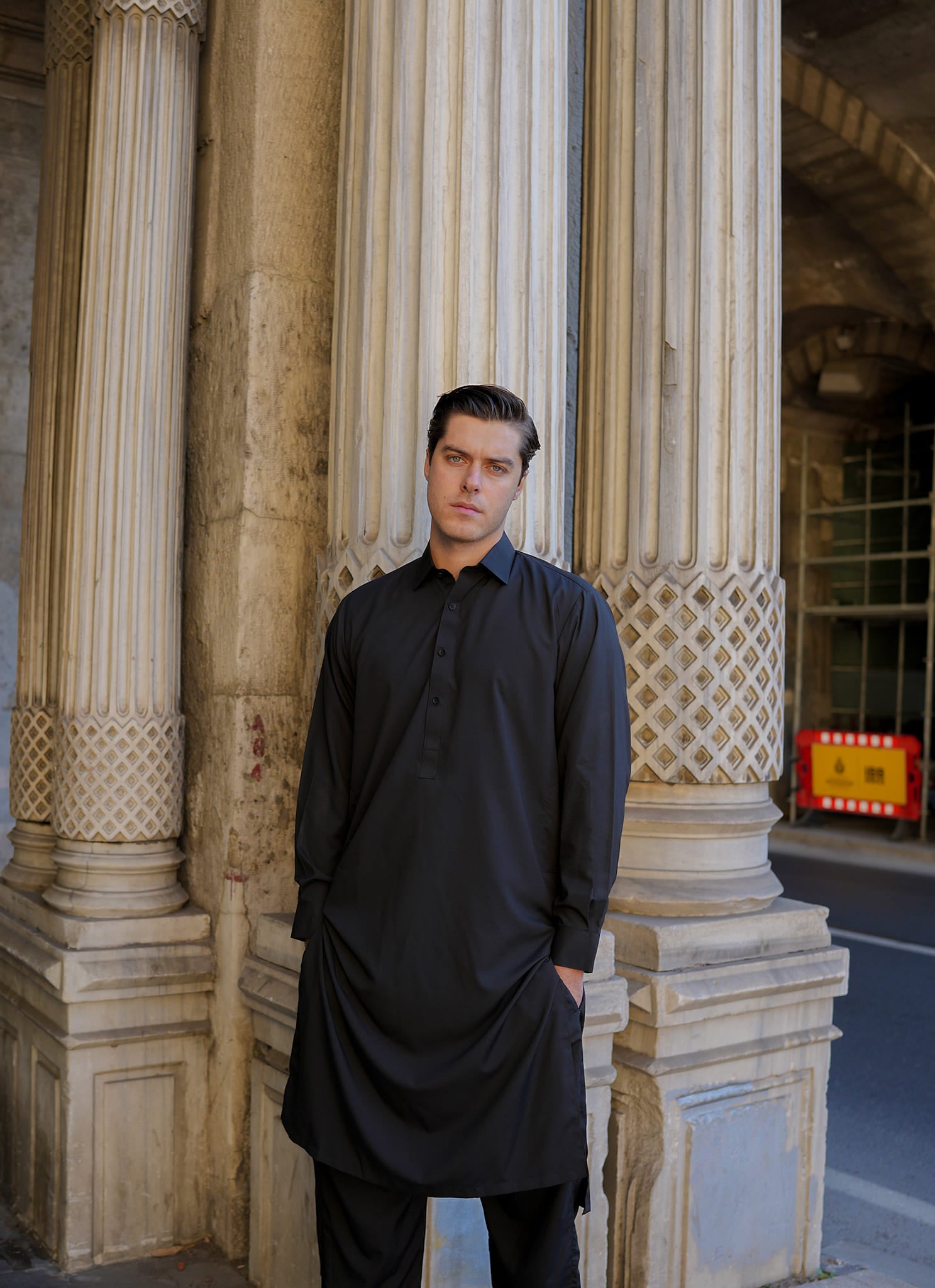 Sheikh Gulzar Fabrics Istanbul Noir — premium unstitched black fabric styled on model near architectural pillars, luxury men’s shalwar kameez fabric Pakistan.