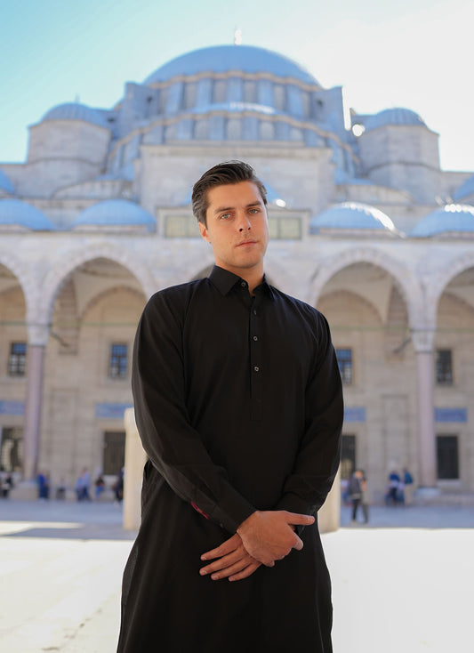 Sheikh Gulzar Fabrics Midnight Shine — premium unstitched black fabric styled on model in mosque courtyard, luxury shalwar kameez fabric Pakistan.