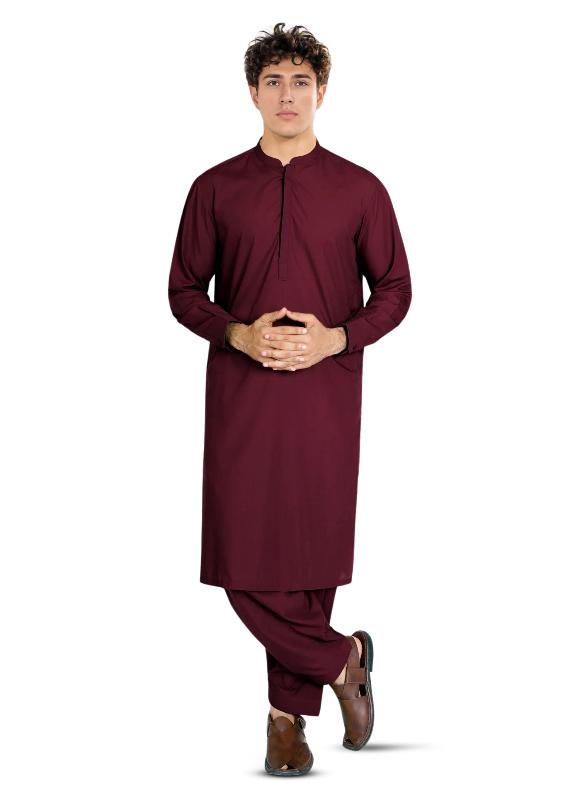 A person standing and posing in a traditional maroon-colored outfit with a shiny and matte finish. Sheikh Gulzar Fabrics Narkins Blended — premium dual-effect cherry red unstitched fabric styled on model, luxury men’s shalwar kameez fabric Pakistan.