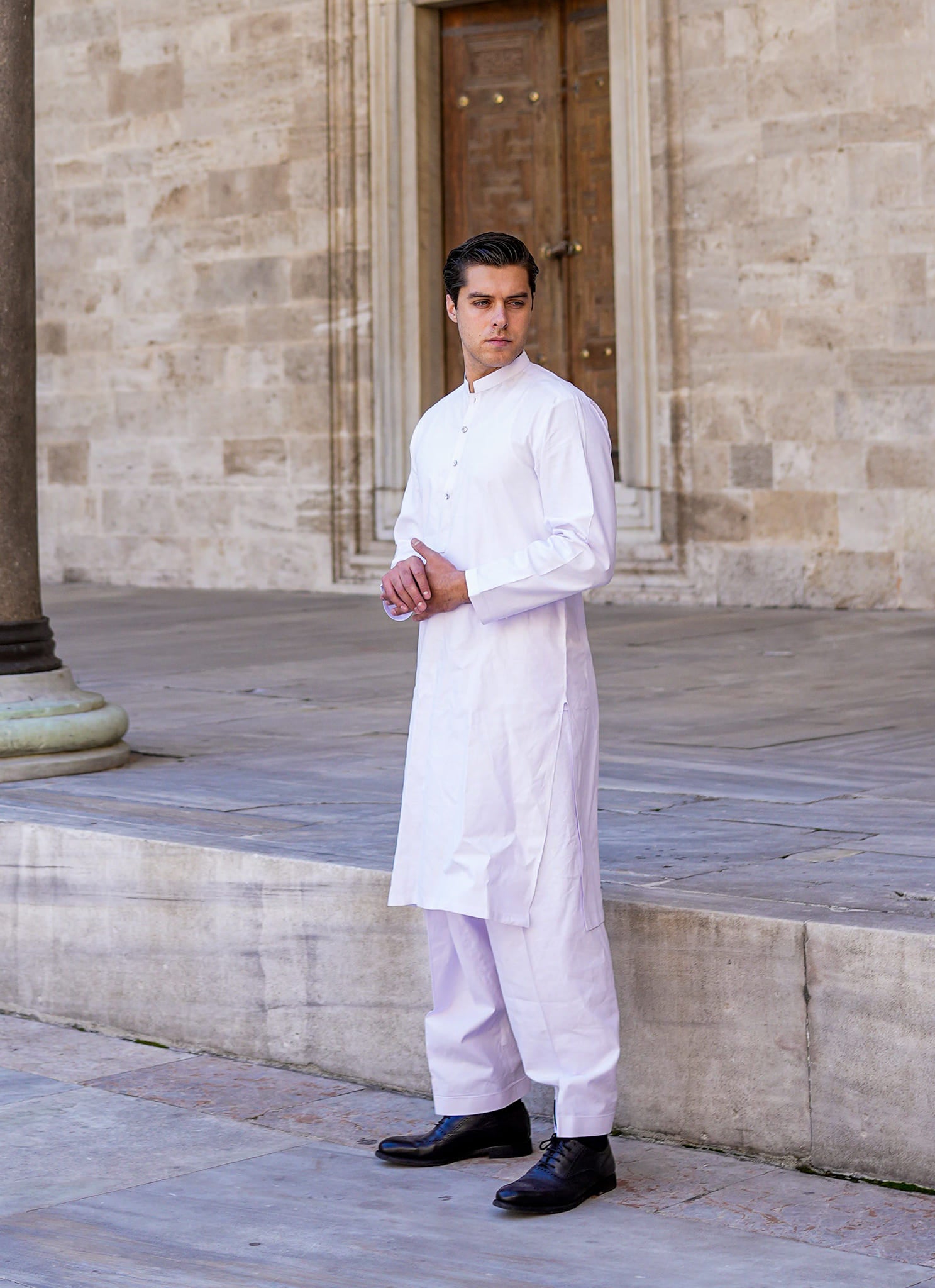 Sheikh Gulzar Fabrics White Sultan — premium unstitched white fabric showcased in traditional kurta style near heritage archway, elegant men’s fabric Pakistan.